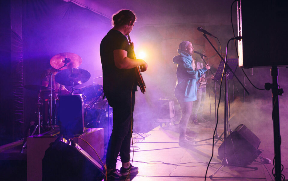 Musicians performing on stage with purple lighting and haze.