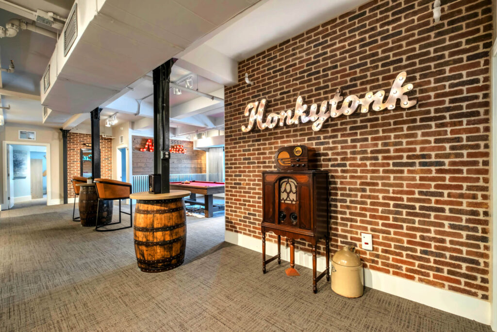 Modern recreational room with "Honkytonk" neon sign, brick walls, vintage radio, and a pool table.