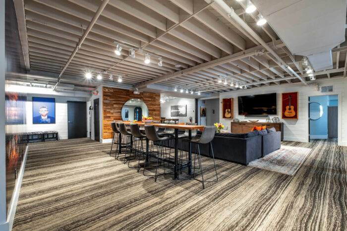 Modern office lounge with high bar stools, a sofa, guitars on the wall, and a TV.