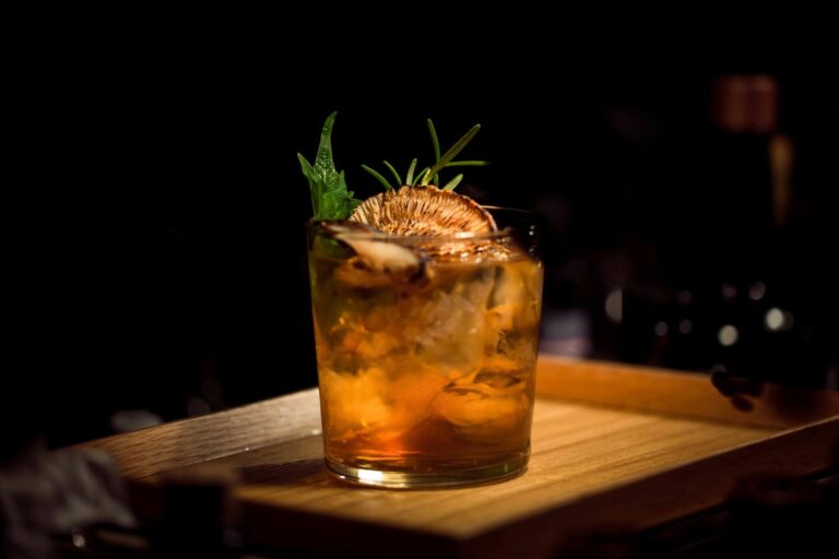 Iced cocktail with garnish on a wooden bar, moody lighting.
