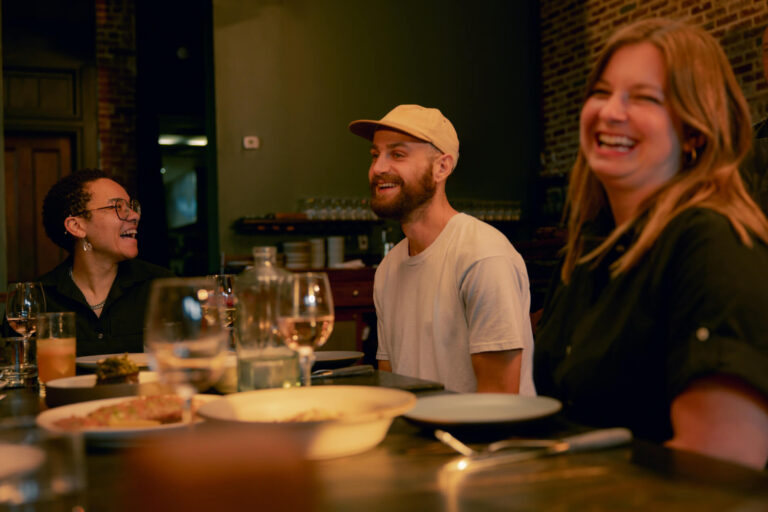 Three people dining at a table with food and drinks in a cozy restaurant setting.