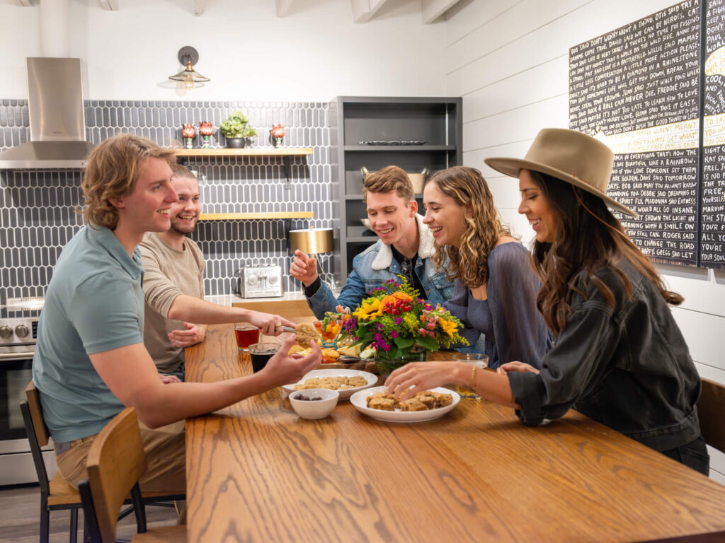 Group of People seated at a dining table with food and flowers, inside a stylish kitchen.