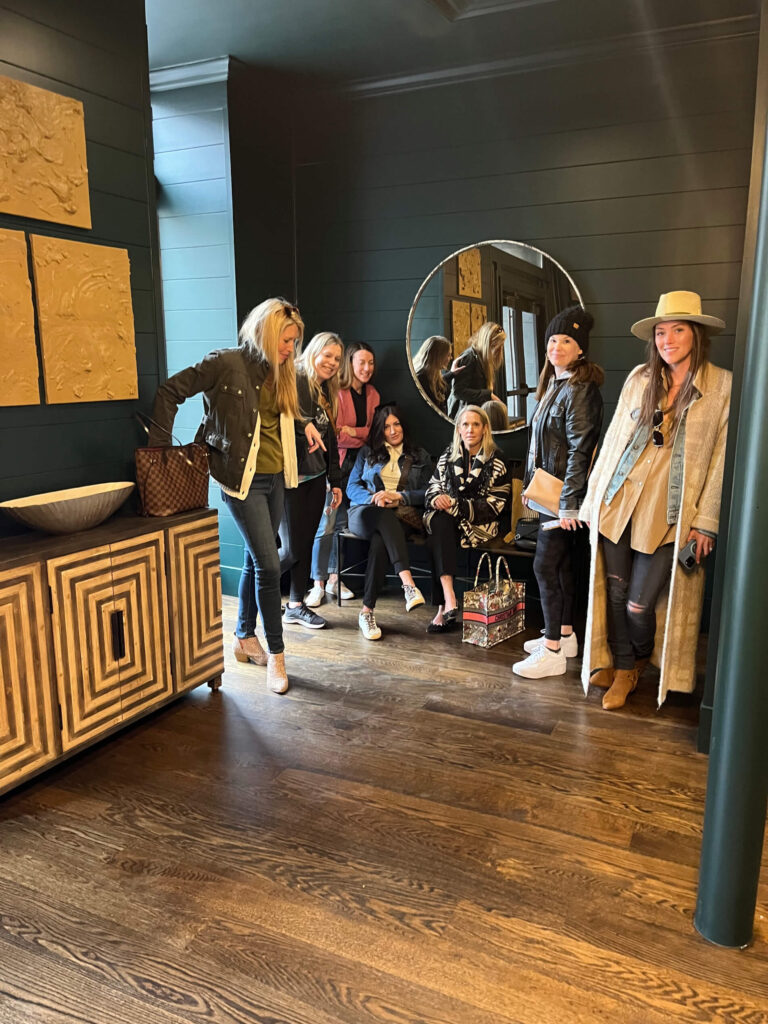 Group of people standing and sitting in a stylish interior with dark walls and a mirror.
