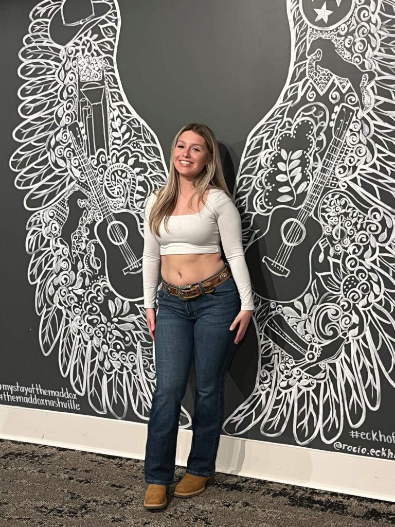 Person standing in front of a black-and-white mural with intricate wing designs.