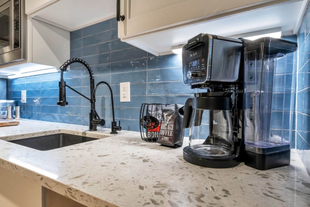 Modern kitchen counter with a coffee machine, bag of coffee beans, and sink with a black faucet.