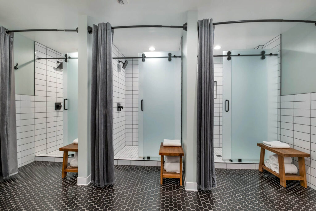 Modern shower area with frosted glass doors, gray curtains, and wooden benches.