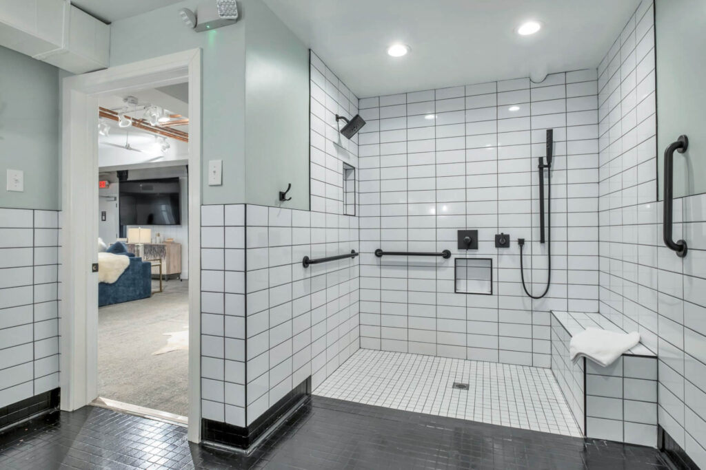 Modern bathroom with white subway tiles, black accents, and accessibility handrails.
