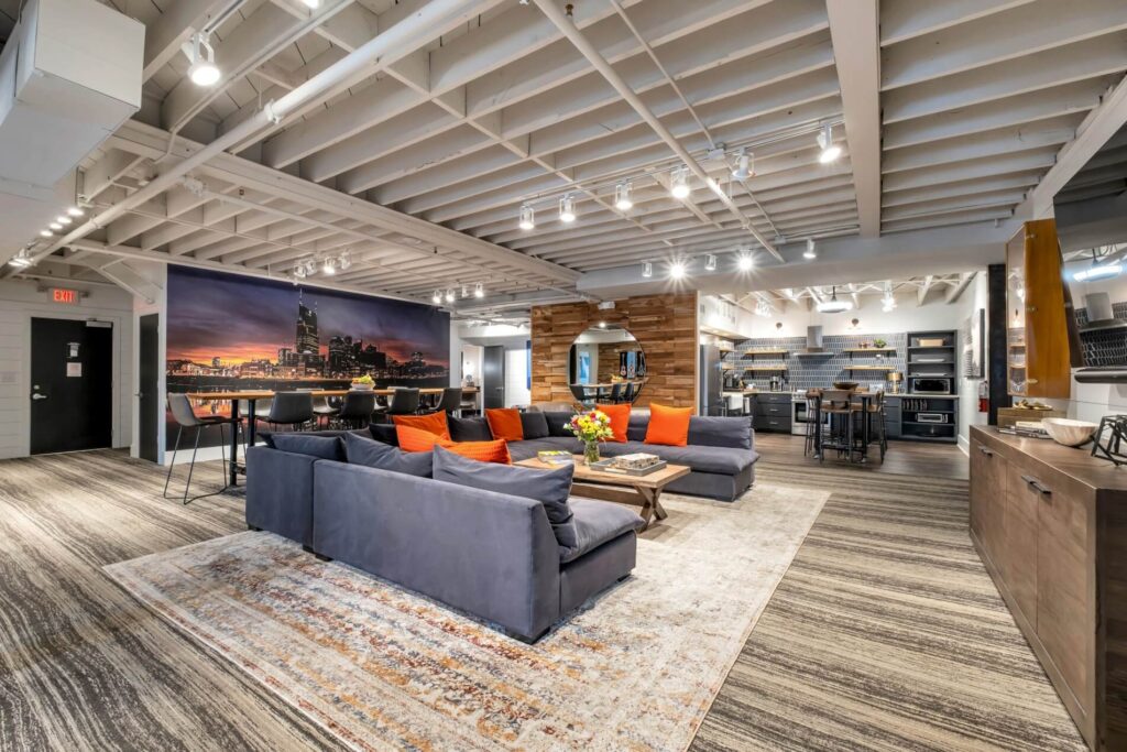 Modern living room with sofas and a large cityscape mural, adjacent to an open kitchen.