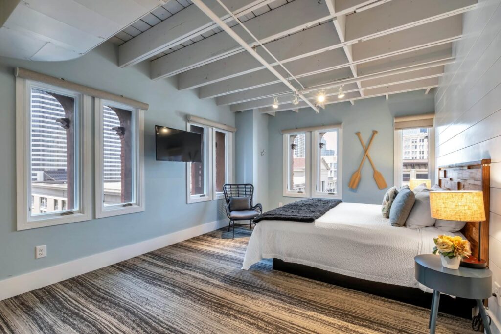 Modern bedroom with exposed beams, large windows, a bed, wall-mounted TV, and decorative oars.