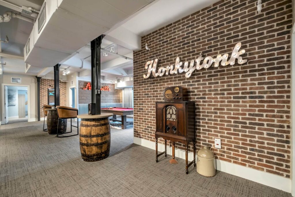 Industrial-style room with "Honkytonk" in lights on a brick wall, antique radio, barrel table.