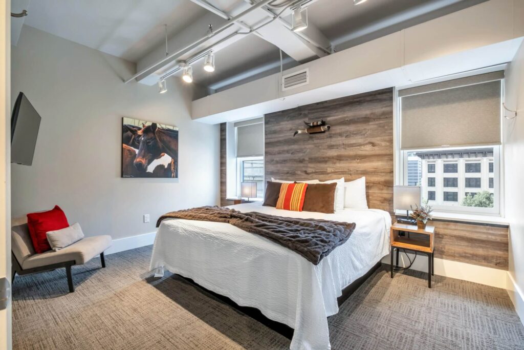 Modern bedroom with a white bed, wooden wall accent, track lighting, and a horse painting.