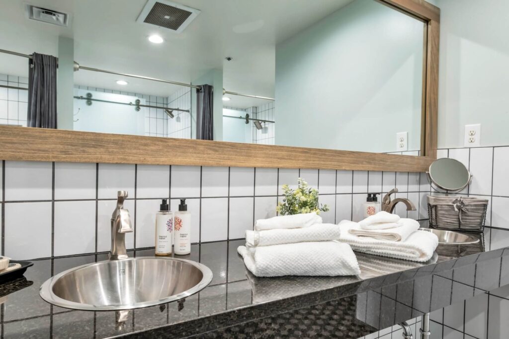 Modern bathroom with steel sink, white towels, and large mirror.