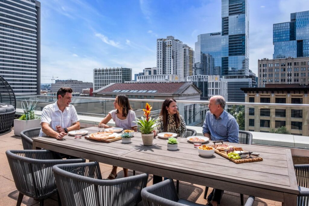 Four people dining on a rooftop patio with a city skyline background.