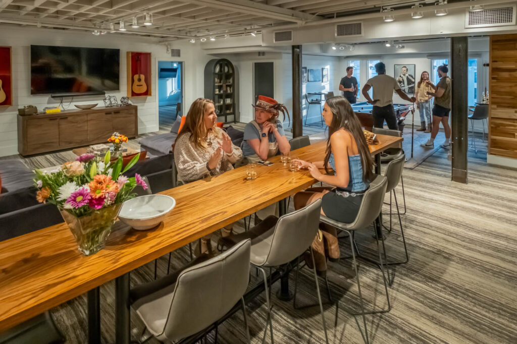 A cozy modern lounge with people socializing, playing foosball, and seated at a wooden table.
