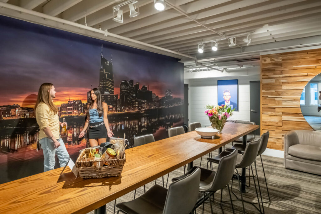 Two people chatting in a modern room with a cityscape mural and stylish wooden furnishings.