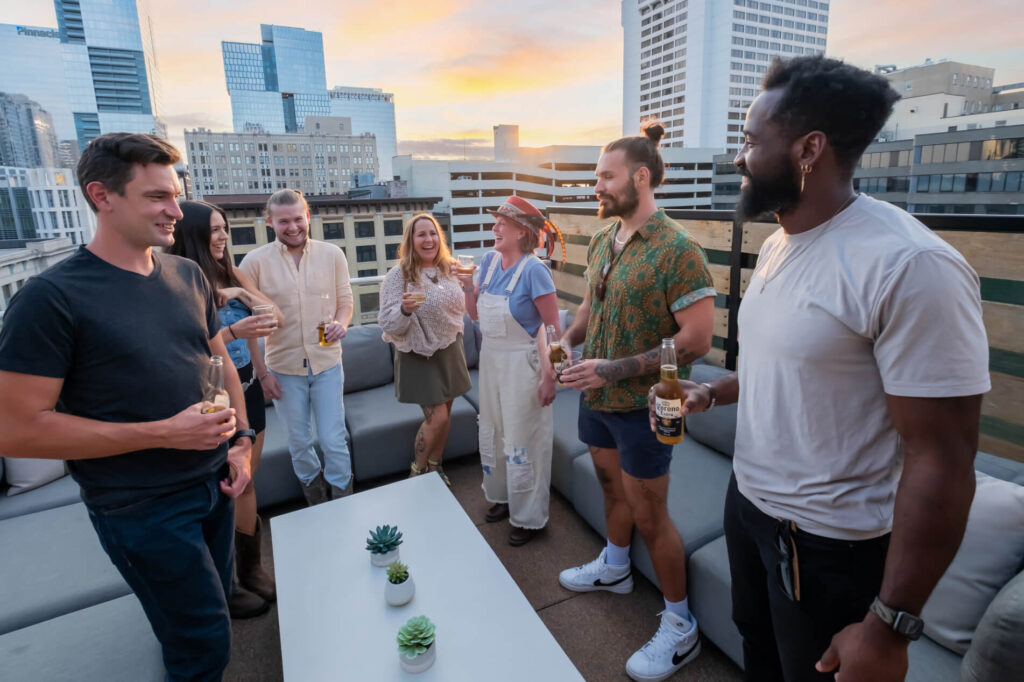 Group of people socializing on a rooftop at sunset with cityscape in the background.