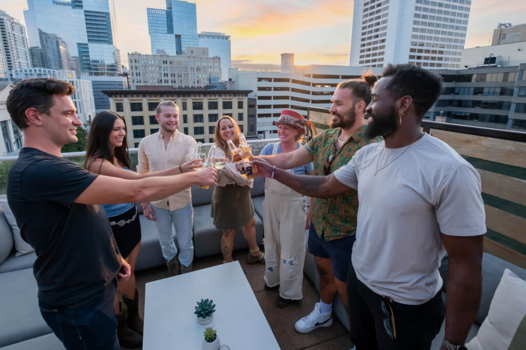 Group of friends toasting drinks at a rooftop gathering during sunset.
