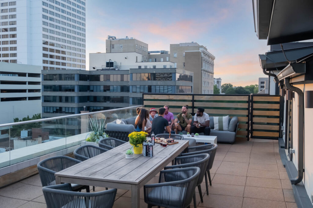 Group of people enjoying a rooftop gathering at dusk with city skyline in the background.