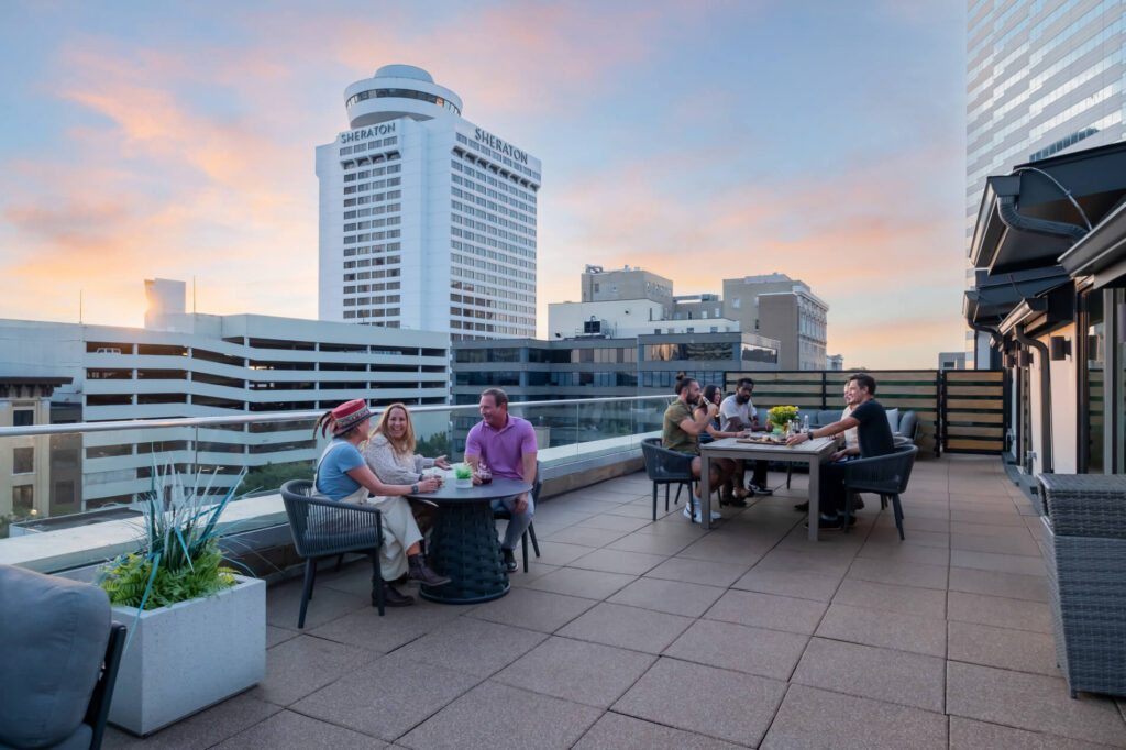 Rooftop gathering with people dining at sunset, city buildings in the background.