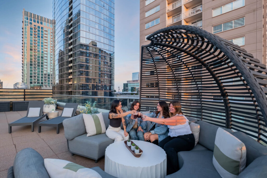 Group of people toasting on a rooftop patio with modern furniture and cityscape background.