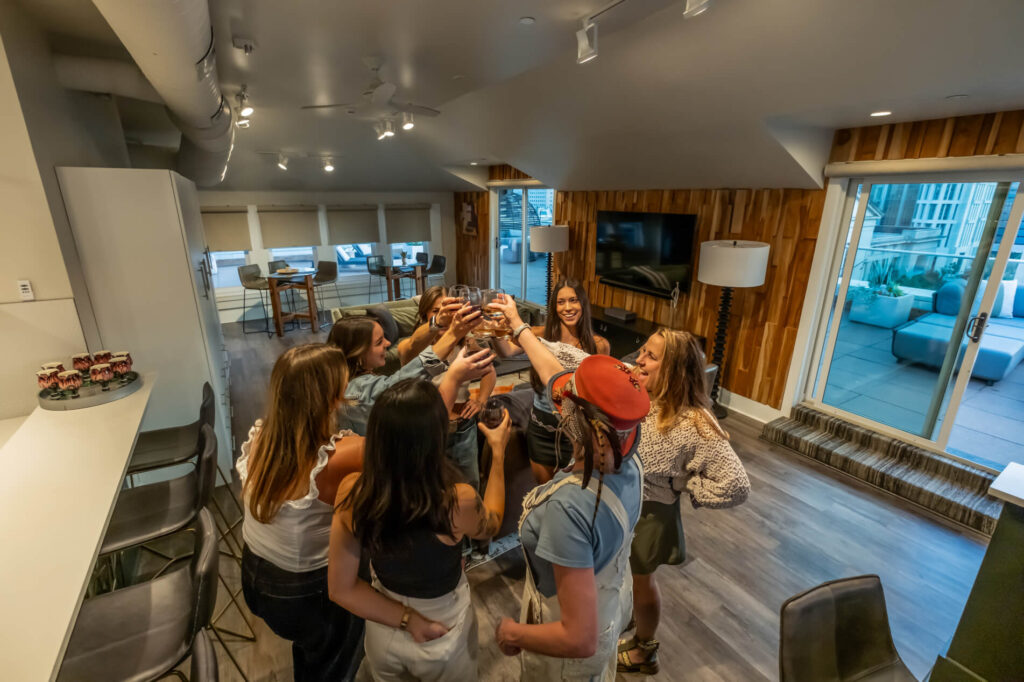 Group of people toasting in a modern living room with desserts on the counter.
