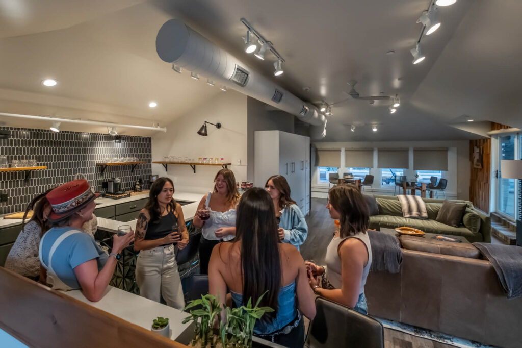 Group of people socializing in a modern kitchen with a seating area in the background.