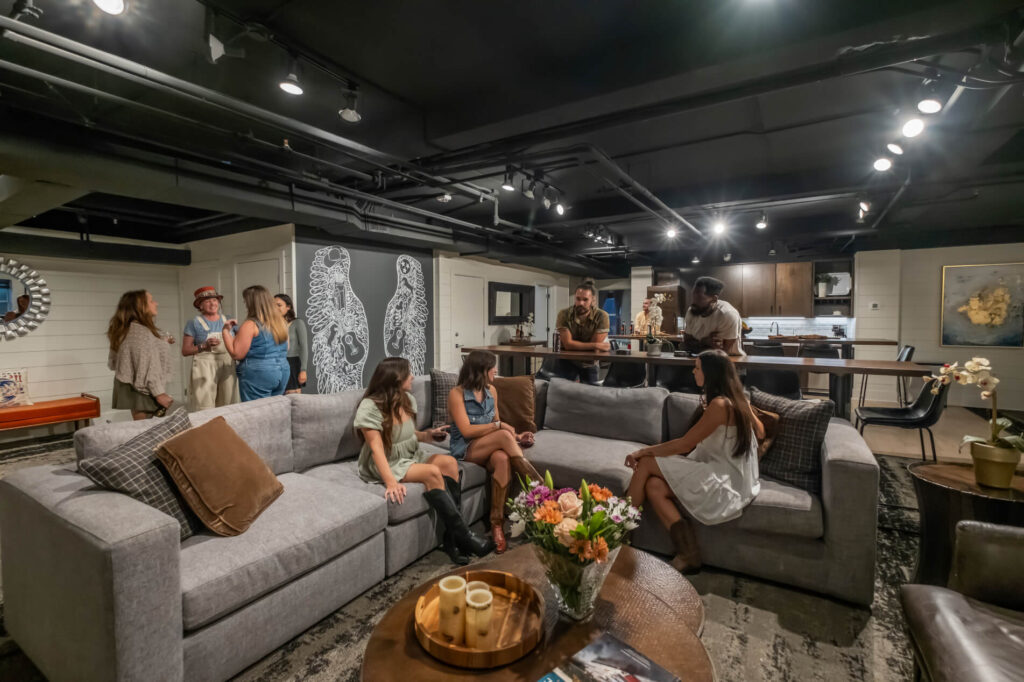 Modern living room with people socializing and kitchen area in the background.