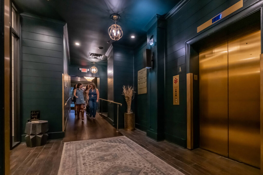 Dark modern hallway with elegant lighting, an elevator door, and people walking.
