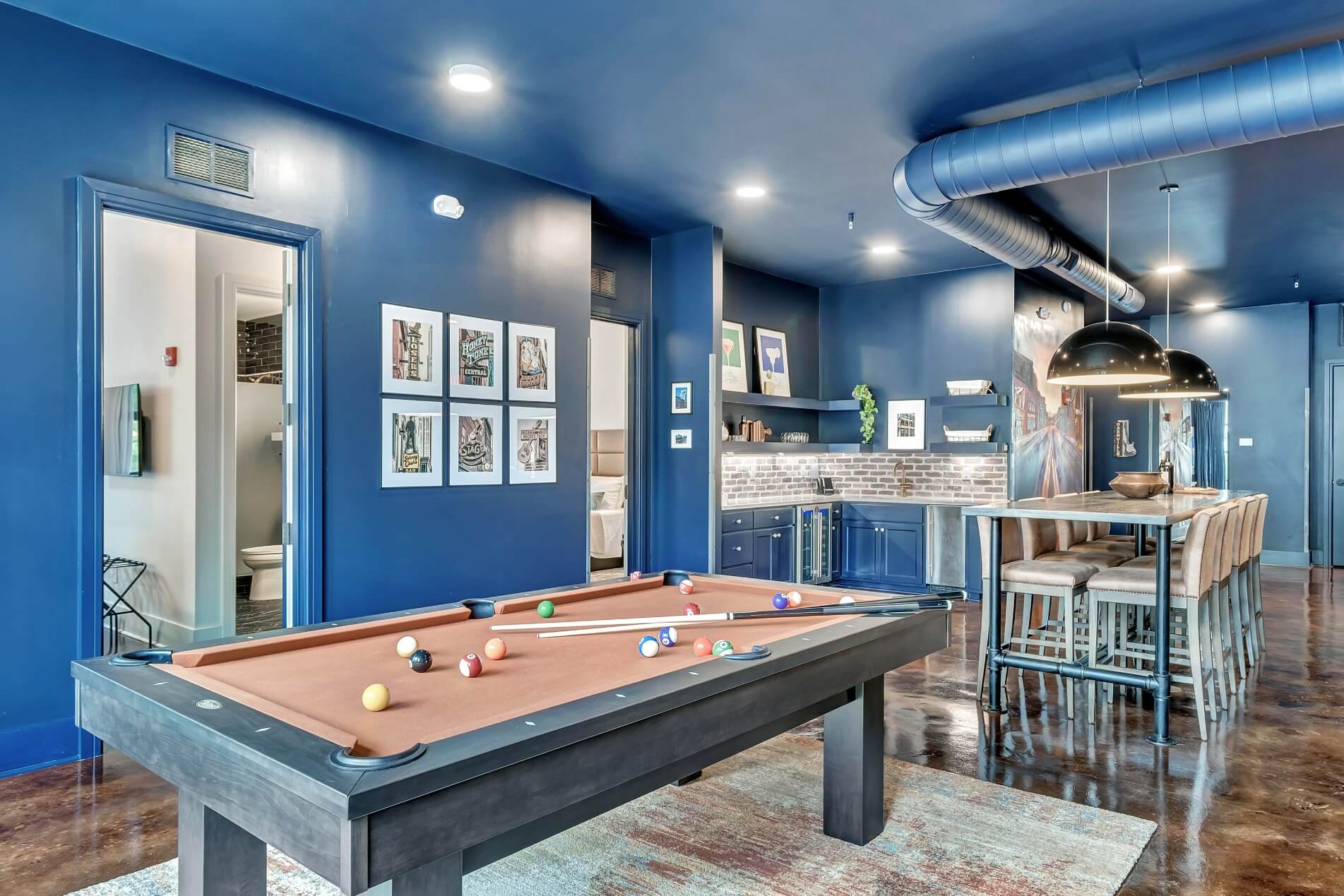 A game room with a pool table, kitchenette, and bar stools.